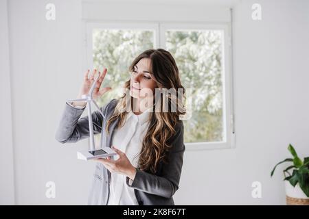 Weibliche Unternehmerin, die im Büro mit Windturbinenmodell steht Stockfoto