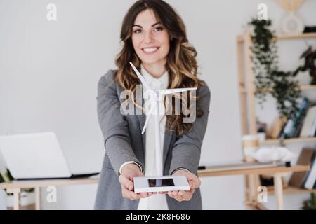 Lächelnde Unternehmerin mit Windturbinenmodell im Büro Stockfoto