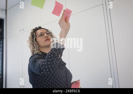 Reife Geschäftsfrau klebt Haftnotizen im Büro Stockfoto