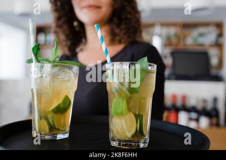 Junge Kellnerin mit Tablett serviert Cocktailgetränke im Restaurant Stockfoto