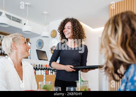 Eine fröhliche Kellnerin mit Tablett sprach mit den Gästen im Restaurant Stockfoto