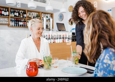 Fröhliche Kellnerin, die den Gästen im Restaurant Cocktails serviert Stockfoto