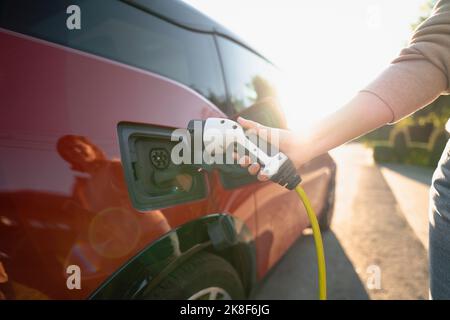 Hand einer Frau, die das Ladegerät an der Ladestation des Fahrzeugs in ein Elektroauto steckt Stockfoto