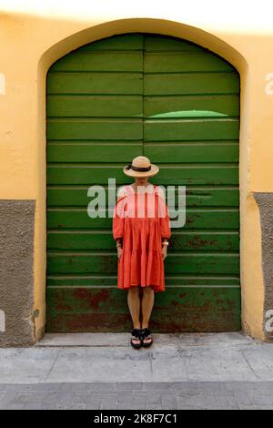 Ältere Frau in rotem Kleid und Sonnenhut vor der grünen Tür Stockfoto