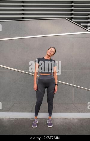 Reife Frau macht Aufwärm-Übung vor der Wand Stockfoto
