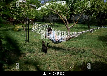 Frau, die in der Hängematte mit Katze im Garten liegt Stockfoto