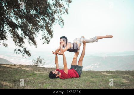 Junger Mann und junge Frau machen acroyoga auf dem Berg Stockfoto
