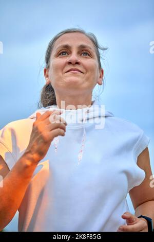 Entschlossene Frau mit Kapuzenhemd beim Joggen vor dem Himmel Stockfoto