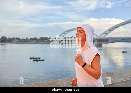 Frau trägt Kapuzenhemd beim Joggen am Fluss Stockfoto