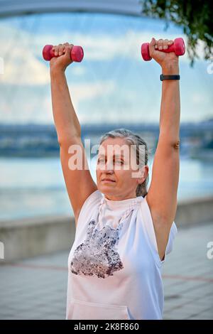 Reife Frau beim Heben von Gewichten im Park Stockfoto