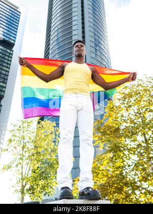 Mann mit Regenbogenfahne vor einem modernen Wolkenkratzer Stockfoto