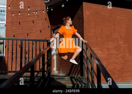 Frau in orangefarbenem Kleid, die auf dem Treppengeländer balanciert Stockfoto