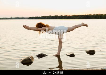 Frau, die eine Kriegerpose praktiziert, inmitten von Felsen im See Stockfoto