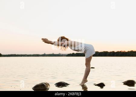 Frau in weißem Kleid beim Training am Seeufer Stockfoto