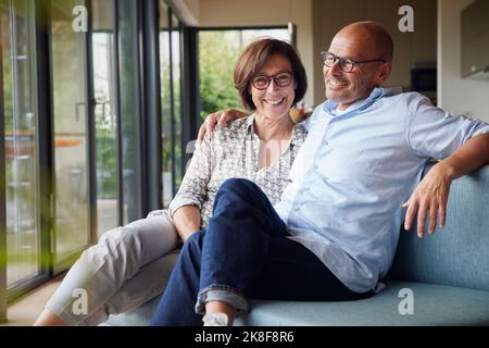 Fröhliches Seniorenpaar, das zu Hause auf dem Sofa sitzt Stockfoto