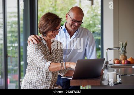 Glückliches Seniorenpaar, das zu Hause einen Laptop benutzt Stockfoto