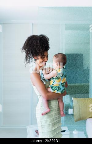 Glückliche Frau, die zu Hause einen kleinen Jungen im Schlafzimmer trägt Stockfoto