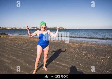 Lächelnde ältere Frau, die am Strand Muskeln anbiegend Stockfoto