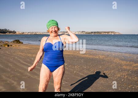 Glückliche ältere Frau, die am Strand Muskeln anbiegend Stockfoto