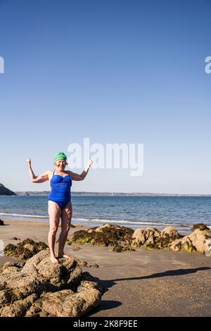 Frau, die auf Felsen steht und Muskeln am Strand beugt Stockfoto