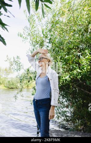 Lächelnde Frau mit erhobener Hand in der Nähe von Pflanzen Stockfoto