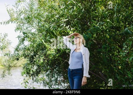 Lächelnde Frau, die die Augen vor den Pflanzen abschirmt Stockfoto