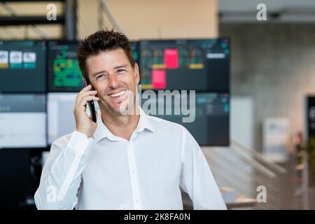 Glücklicher Geschäftsmann im Gespräch auf dem Handy vor Computer-Monitore Stockfoto