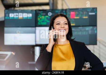 Glückliche Geschäftsfrau im Gespräch auf dem Handy vor Computer-Monitore Stockfoto