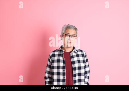 Der 40s-jährige asiatische Mann, der auf dem rosa Hintergrund mit legerer Kleidung stadiert. Stockfoto