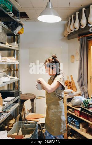 Potter untersucht Keramik, die in der Werkstatt an einem Gestell steht Stockfoto