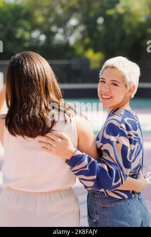 Glückliche nicht-binäre Person mit Freund, der an einem sonnigen Tag steht Stockfoto