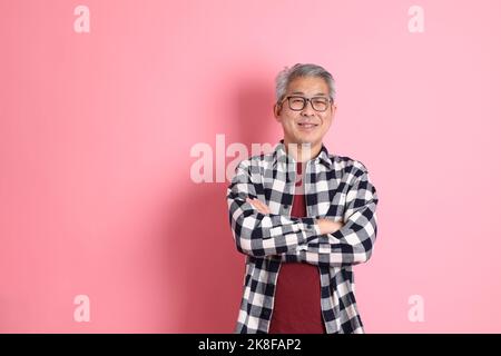 Der 40s-jährige asiatische Mann, der auf dem rosa Hintergrund mit legerer Kleidung stadiert. Stockfoto