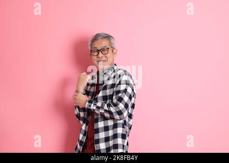 Der 40s-jährige asiatische Mann, der auf dem rosa Hintergrund mit legerer Kleidung stadiert. Stockfoto