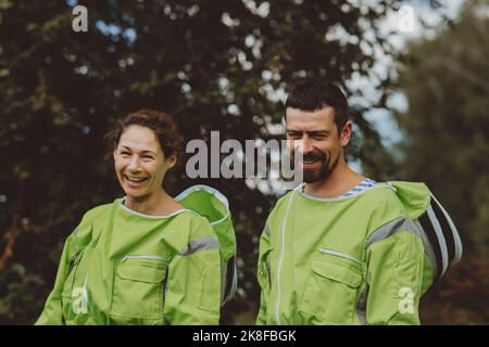 Fröhlicher Imker mit Kollegen in grünen Schutzanzügen Stockfoto