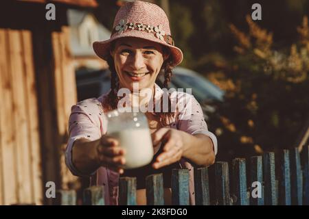 Lächelnde reife Frau, die am Zaun ein Glas mit frischer Milch gibt Stockfoto