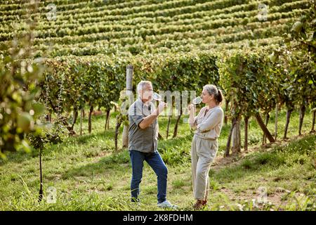 Reifer Mann und Frau trinken Wein im Weinberg Stockfoto