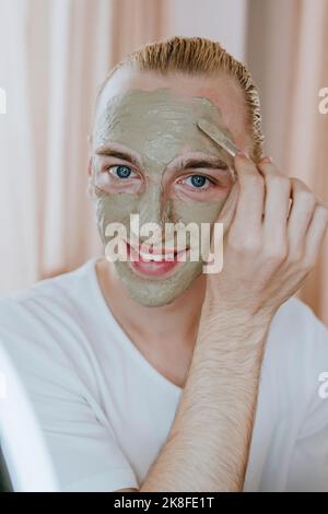 Glücklicher junger Mann, der zu Hause Gesichtsmaske aufführt Stockfoto