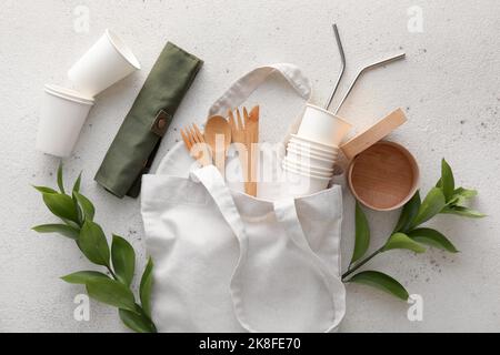 Tragetasche mit Öko Geschirr und Pflanzenzweigen auf weißem Hintergrund Stockfoto