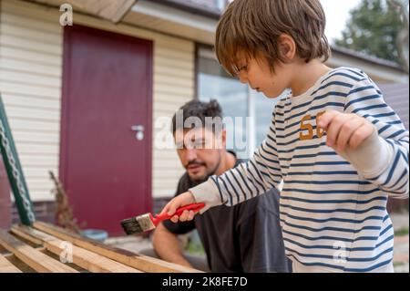 Vater schaut auf Sohn malen Holzschaukel vor dem Haus Stockfoto