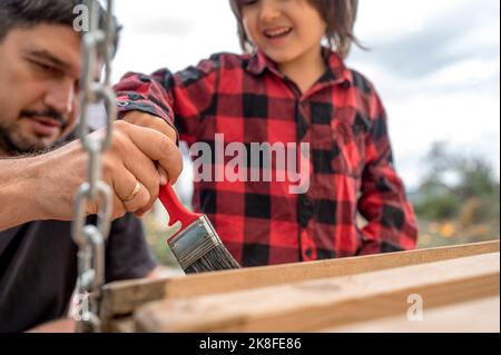 Vater führt Sohn Malerei hölzerne Schaukel Stockfoto