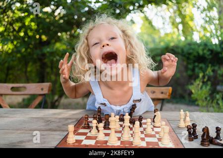 Aufgeregt Mädchen mit Schachbrett auf Tisch im Garten Stockfoto