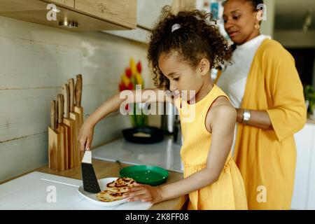 Mädchen hilft Mutter beim Kochen an der Küchentheke Stockfoto