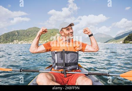 Aufgeregter Mann mit erhobenen Armen im Kajak sitzend Stockfoto