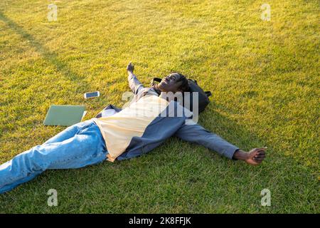 Lächelnder Geschäftsmann mit Mobiltelefon und Laptop, der sich auf dem Rasen entspannt Stockfoto