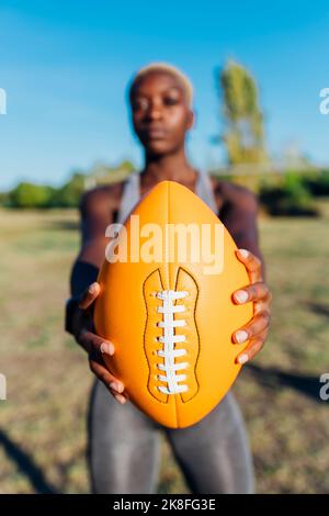 Junge Sportspielerin zeigt American Football an sonnigen Tagen Stockfoto