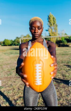 Selbstbewusster Sportspieler, der American Football auf dem Spielfeld hält Stockfoto
