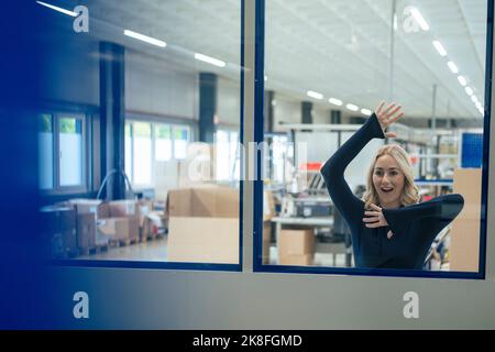 Überraschte Geschäftsfrau, die sich in der Industrie an Glasfenster lehnt Stockfoto