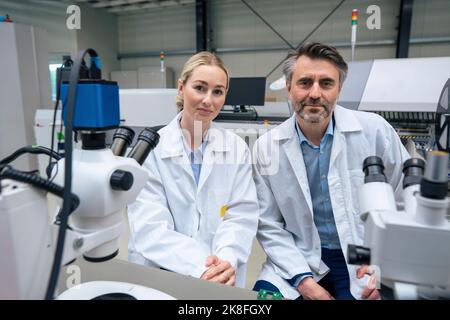 Lächelnde Wissenschaftler im Labormantel sitzen in der Industrie Stockfoto