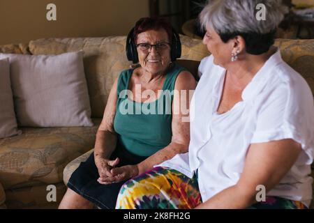 Tochter sitzt mit Mutter, die Kopfhörer trägt Stockfoto