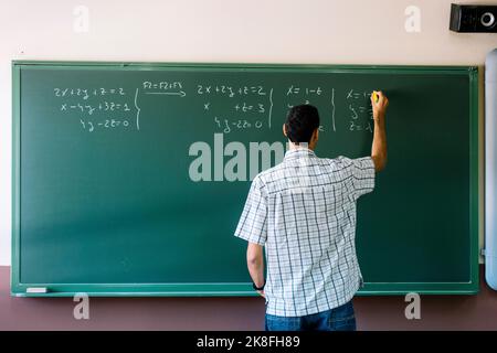 Mathematiklehrer schreibt Formeln auf Tafel im Klassenzimmer Stockfoto